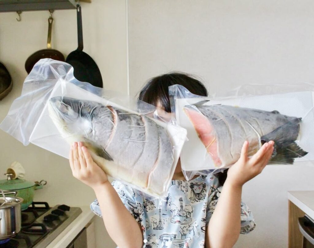 小さな子どもが北海道産の鮭を持ち上げている様子。鮭はじゃがいもや玉ねぎと調理されている。